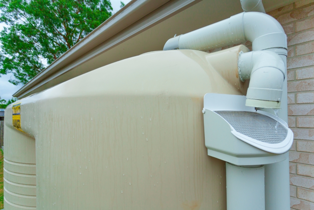 A beige rainwater tank with connected pipes collects rainwater from a rooftop, exemplifying an efficient and eco-friendly solution for using rainwater for garden irrigation.