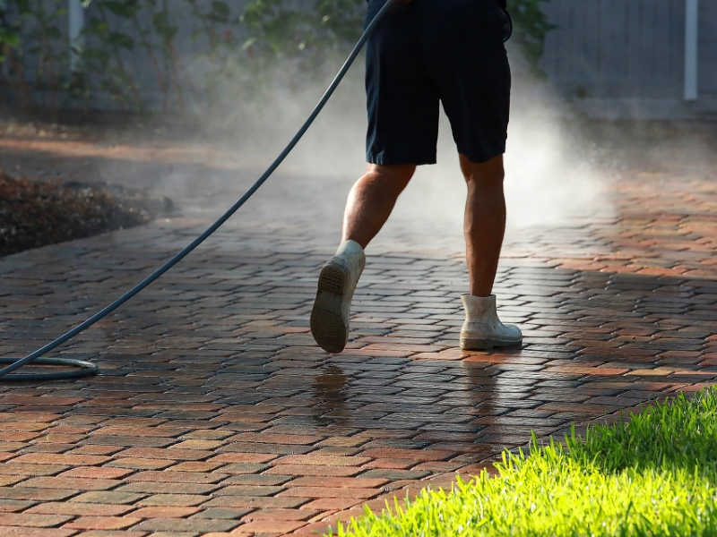 Person power-washing textured pavers, highlighting their slip-resistant properties and maintenance process in a garden setting.