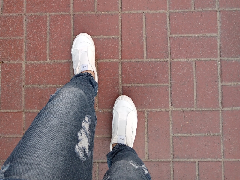 Person wearing white shoes walking on textured pavers with a brick pattern, showcasing slip-resistant surface.