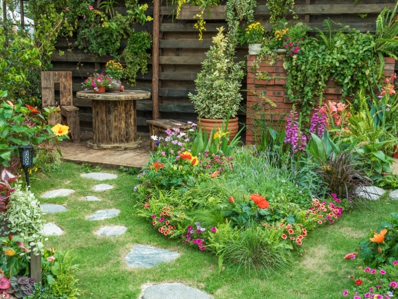 Rustic backyard garden design with wooden furniture, colourful flowers, and stone path for a cosy outdoor setup.