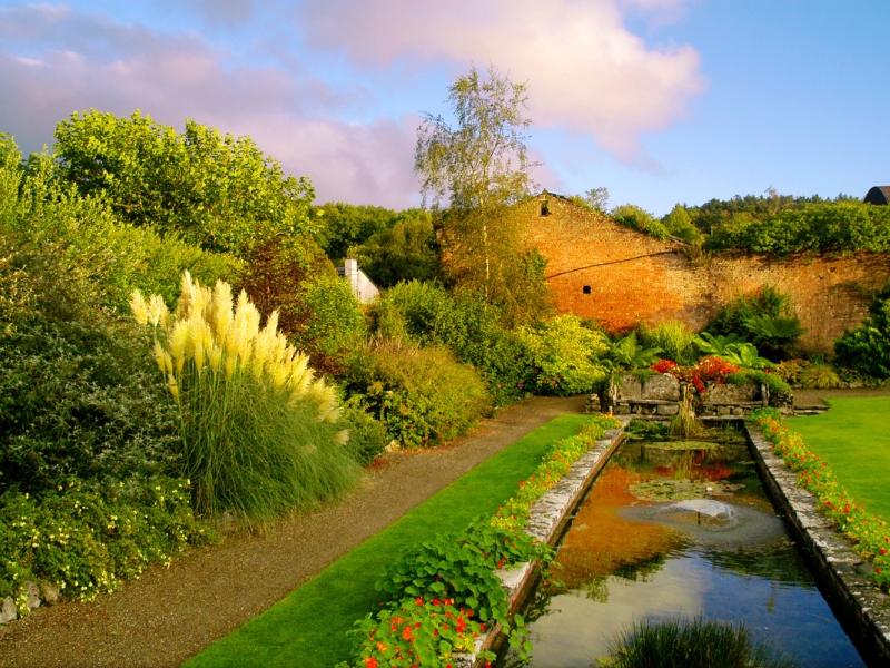 Traditional garden style with colourful plants, tall grasses, brick wall, and a reflective water feature.