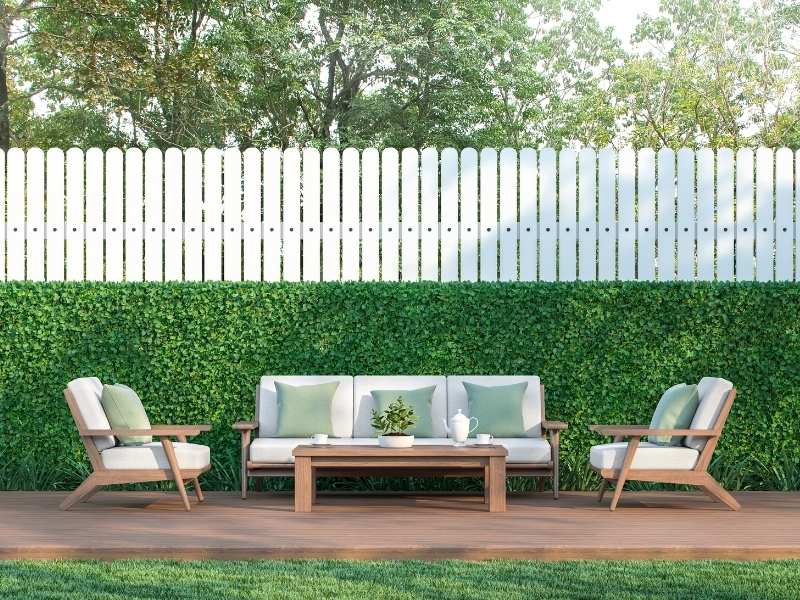 Modern backyard garden design featuring a white fence, greenery, and wooden outdoor seating for relaxation