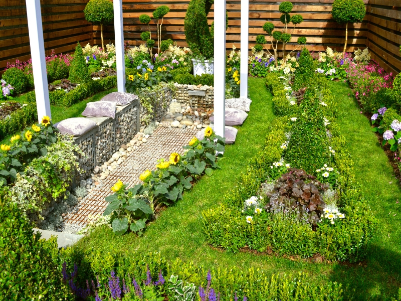 Modern garden style featuring structured flower beds, sunflowers, stone seating area, and decorative plants.