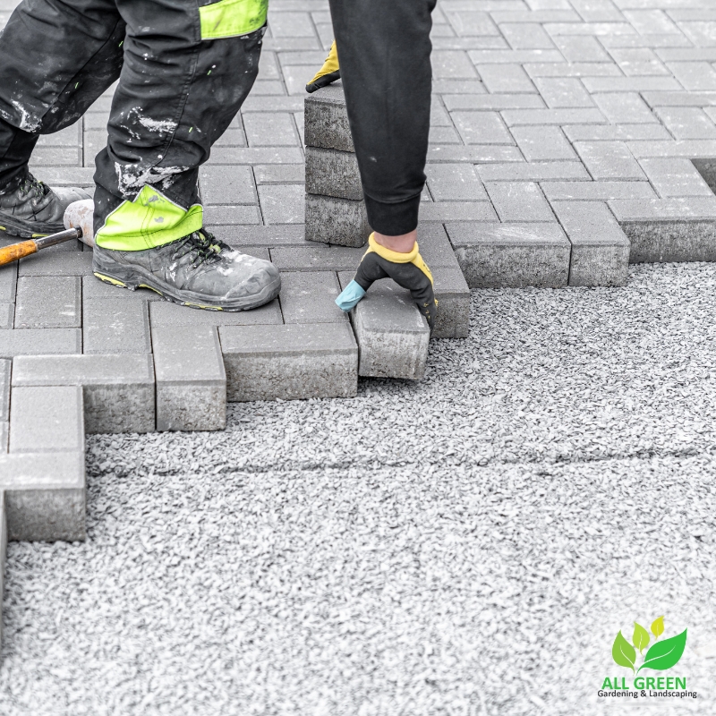 Workers installing grey pavers for driveway paving in Sydney, showing professional paving techniques and tools for a durable, smooth surface.