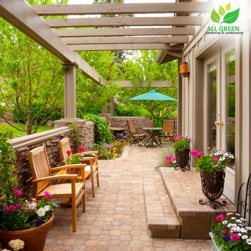 Beautiful patio paving with wooden chairs, vibrant flowers, pergola, and green umbrella, creating a relaxing outdoor garden space.