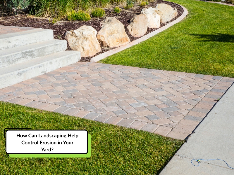 Landscaping for erosion control is evident in this yard with a paved patio, rock-lined mulch bed, and healthy grass. The design demonstrates how landscaping techniques can help manage soil and prevent erosion.