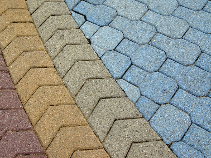 Close-up of curved bands of interlocking concrete pavers—red, tan, grey borders around a blue hexagonal field—showcasing modern paving designs.