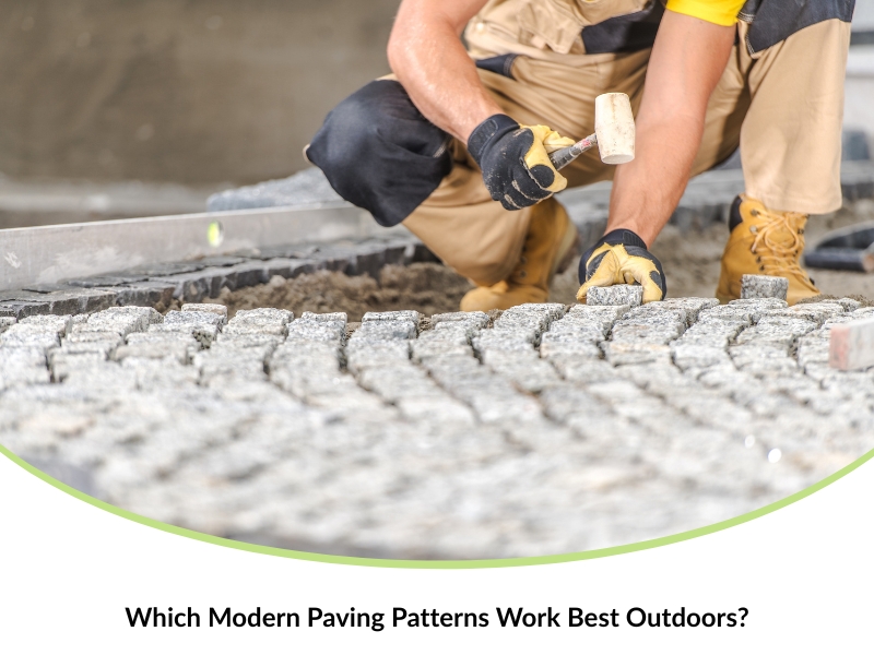 Worker in gloves using a rubber mallet to set small stone pavers on a sand base, showcasing modern paving designs.