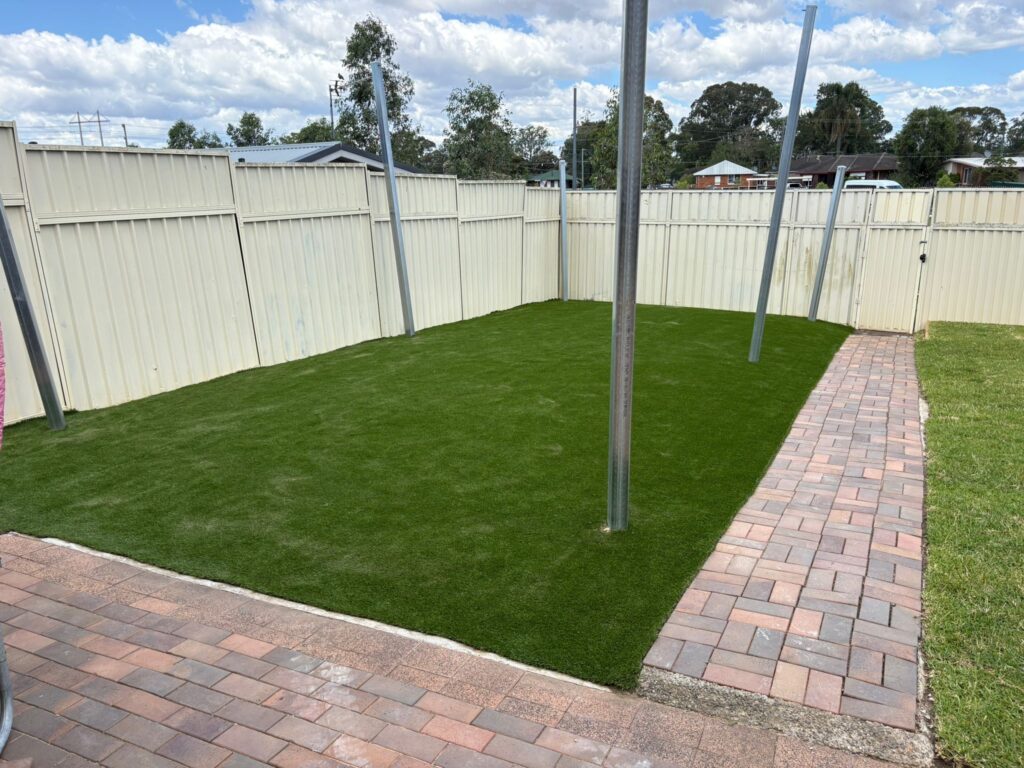 A backyard lawn with fresh green turf, brick paving paths, metal posts, and fencing completed during